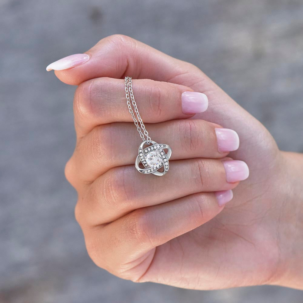 a womans hand holding 14k white gold over stainless steel love knot pendant neckalce