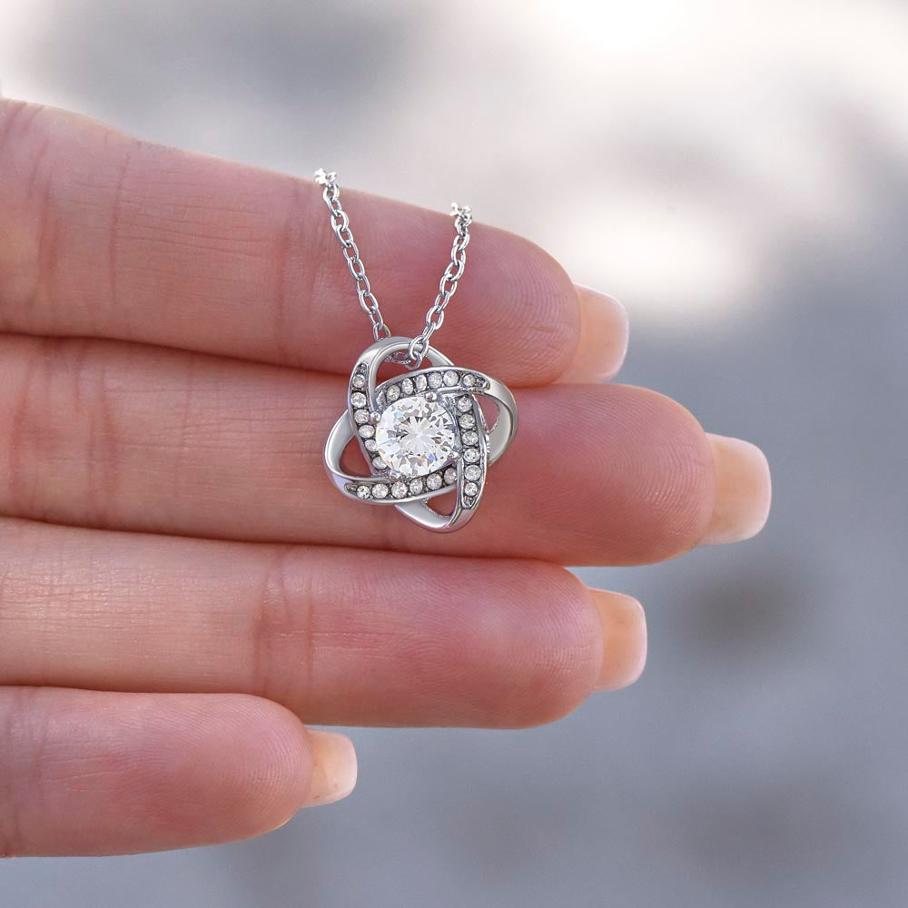 a female hand with a love knot necklace pendnt between her fingers
