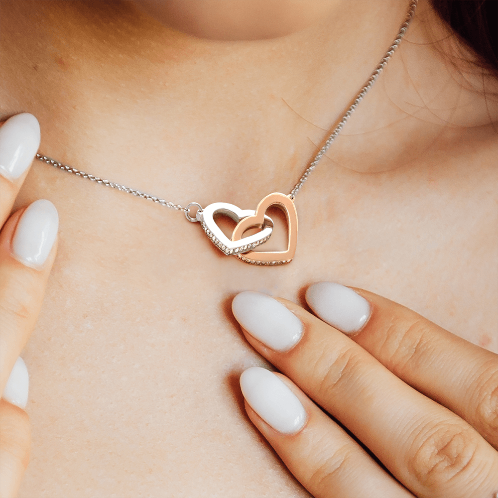 woman wearing a necklace that is 2 interlocking hearts with one heart staoinless steel and one is yello gold finish
