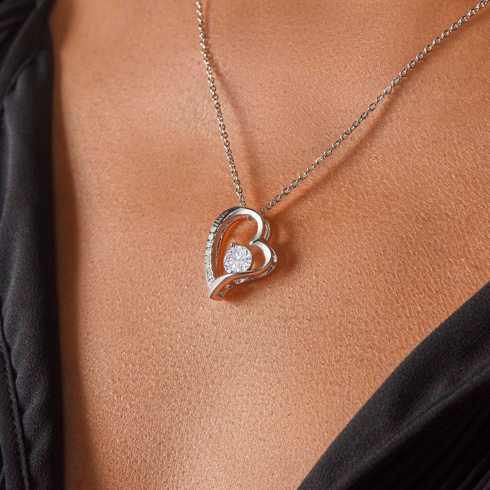 woman wearing a heart pendant necklace on It. 14k white gold finish or 18k yellow gold finish 6.5mm round cut cubic zirconia stone Pendant dimensions: 0.8" (2.2cm) height / 0.7" (1.8cm) width Adjustable chain length: 18" - 22" (45.72cm - 55.88cm) Lobster clasp attachment